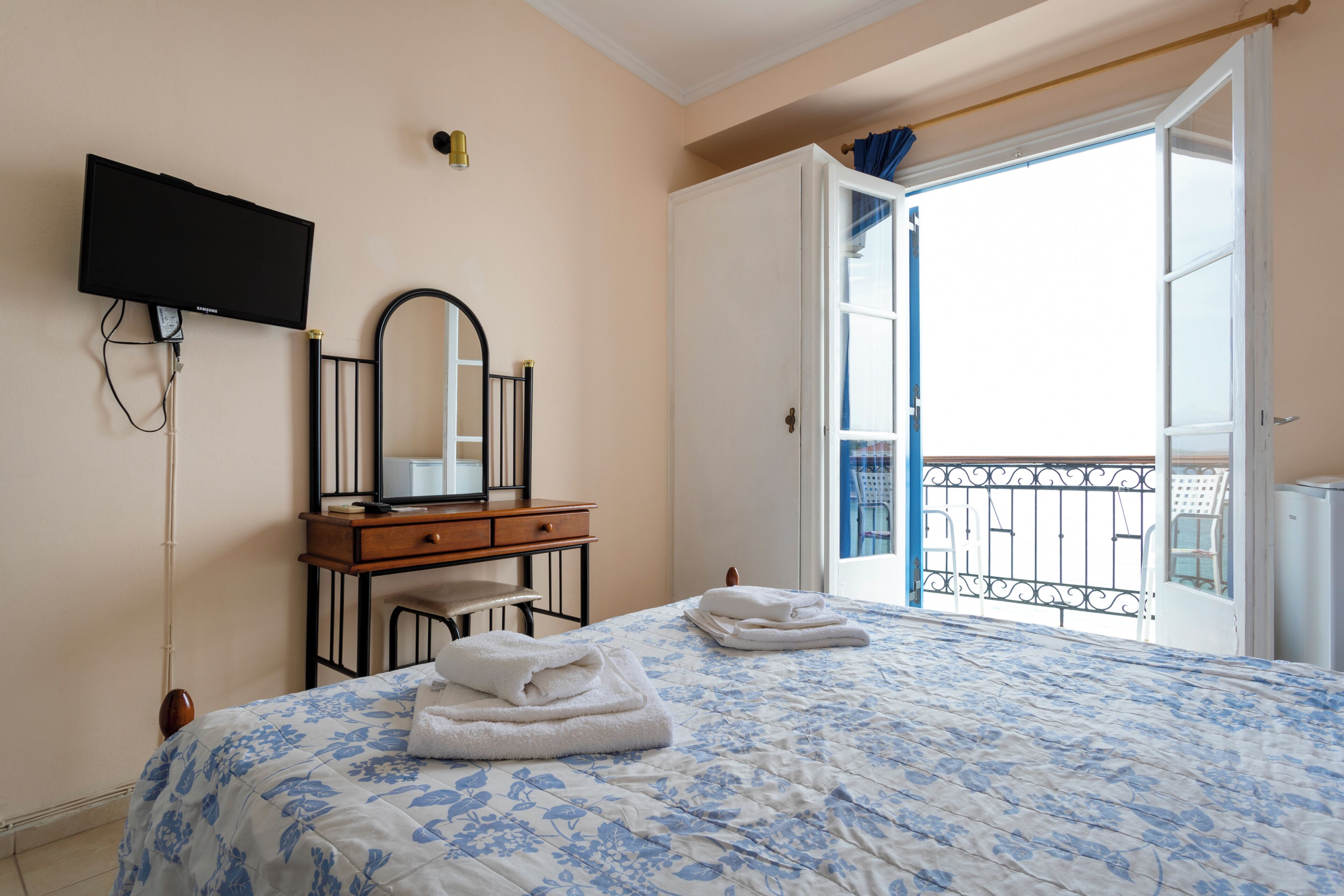 Une chambre à coucher comprenant un lit, une commode, un miroir, un téléviseur et un balcon avec une balustrade.