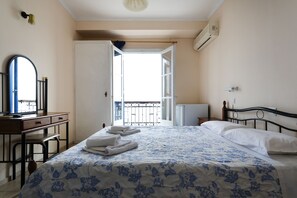 A bedroom with a bed, a desk, a chair, a mirror, and a balcony. - Stelios Hotel (Spetses)