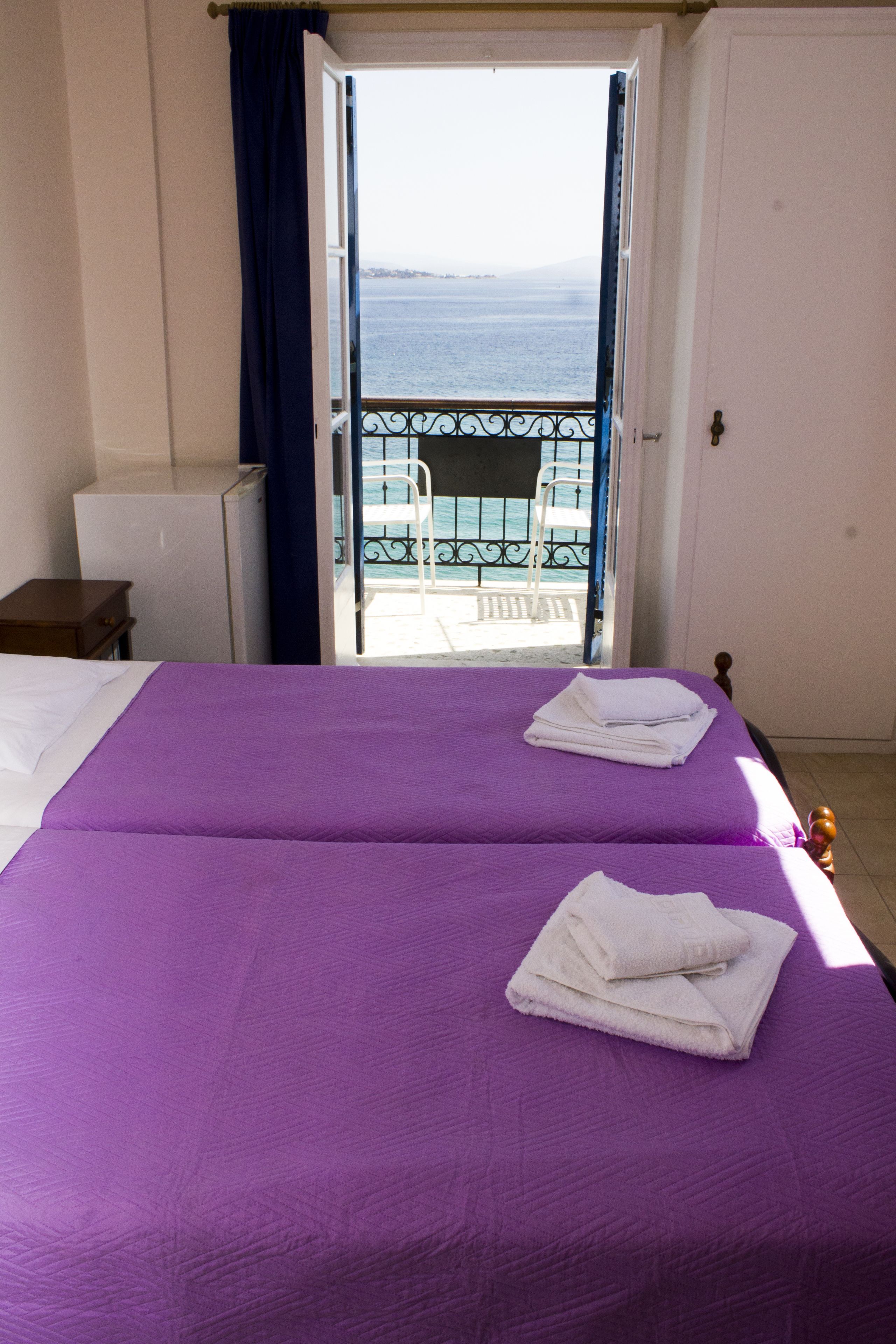 A room with a bed, a small table, and a balcony with a view of the sea.