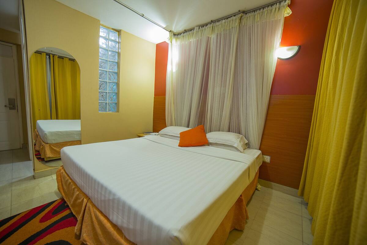 Una habitación de hotel con una cama grande, una ventana con cortinas, un espejo y una mesita de noche.