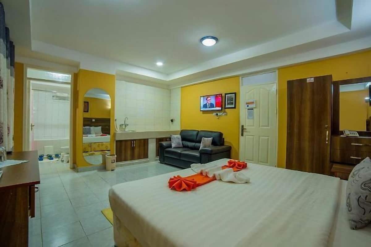 Habitación de hotel con cama, sofá, escritorio, espejo, televisión y baño.
