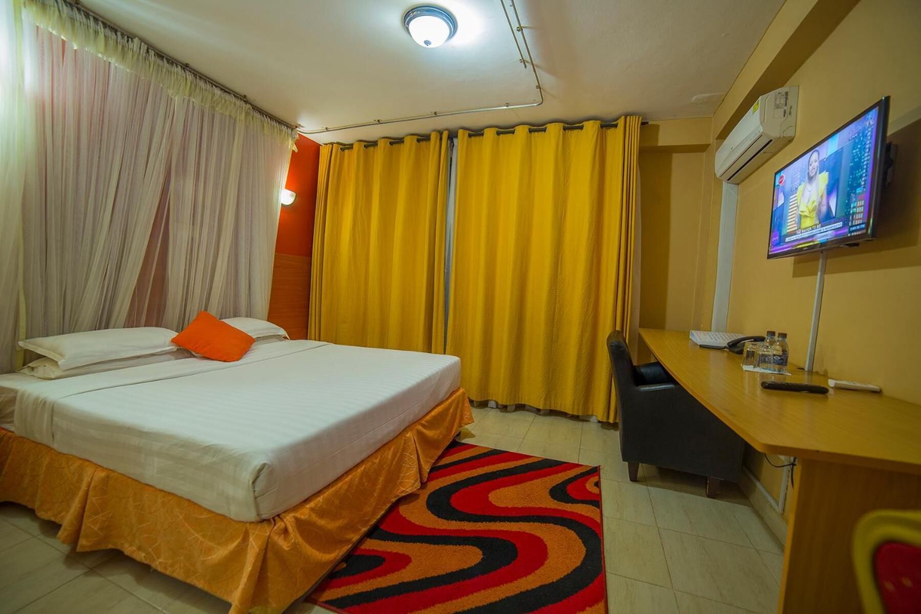 A hotel room with a bed, a desk, a television, and curtains.