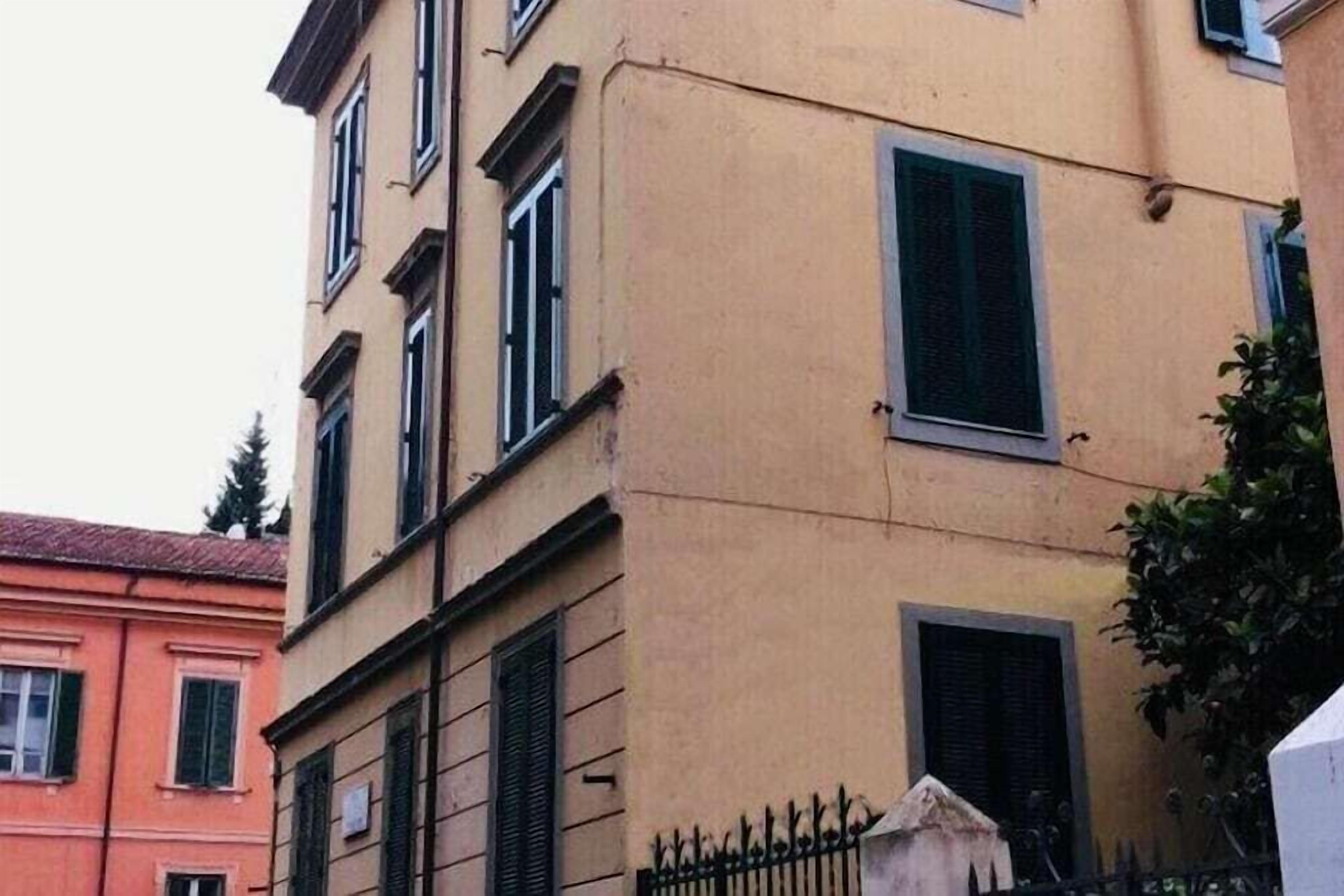 A multi-story building with a beige facade, multiple windows with shutters, and a visible balcony.