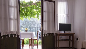 Una stanza con un grande tappeto, una TV su un supporto in legno e un balcone con tavolo e sedie.