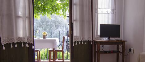 Una habitación con un tapete grande, un televisor sobre un mueble de madera y un balcón con mesa y sillas.