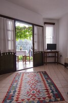 Una habitación con un tapete grande, un televisor sobre un mueble de madera y un balcón con mesa y sillas.