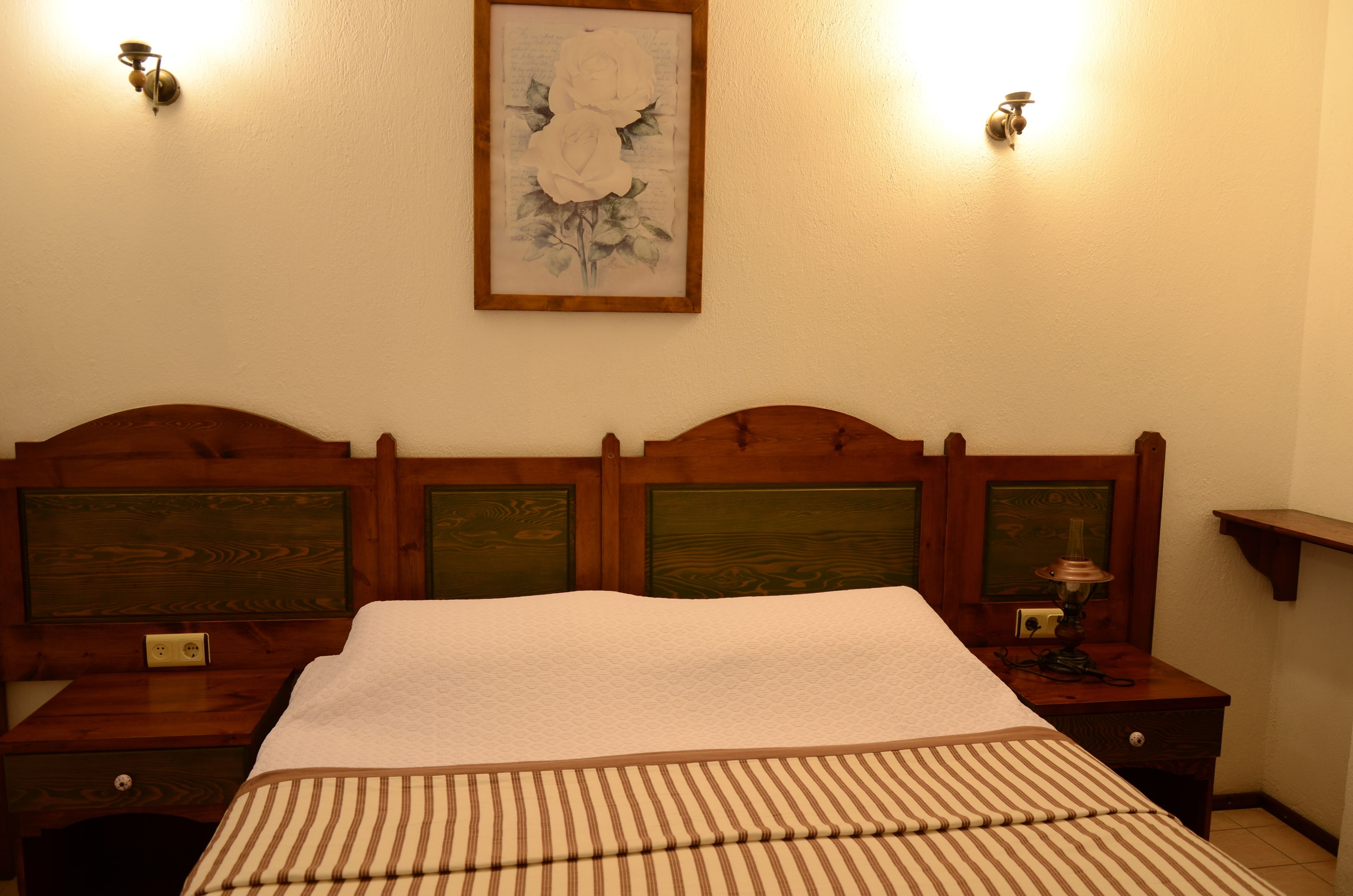 A neatly made bed with a striped bedspread, wooden headboard with green panels, and two bedside tables with lamps.