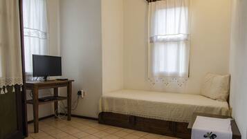 A small, tidy room with a single bed, a TV on a wooden table, and a window with curtains.