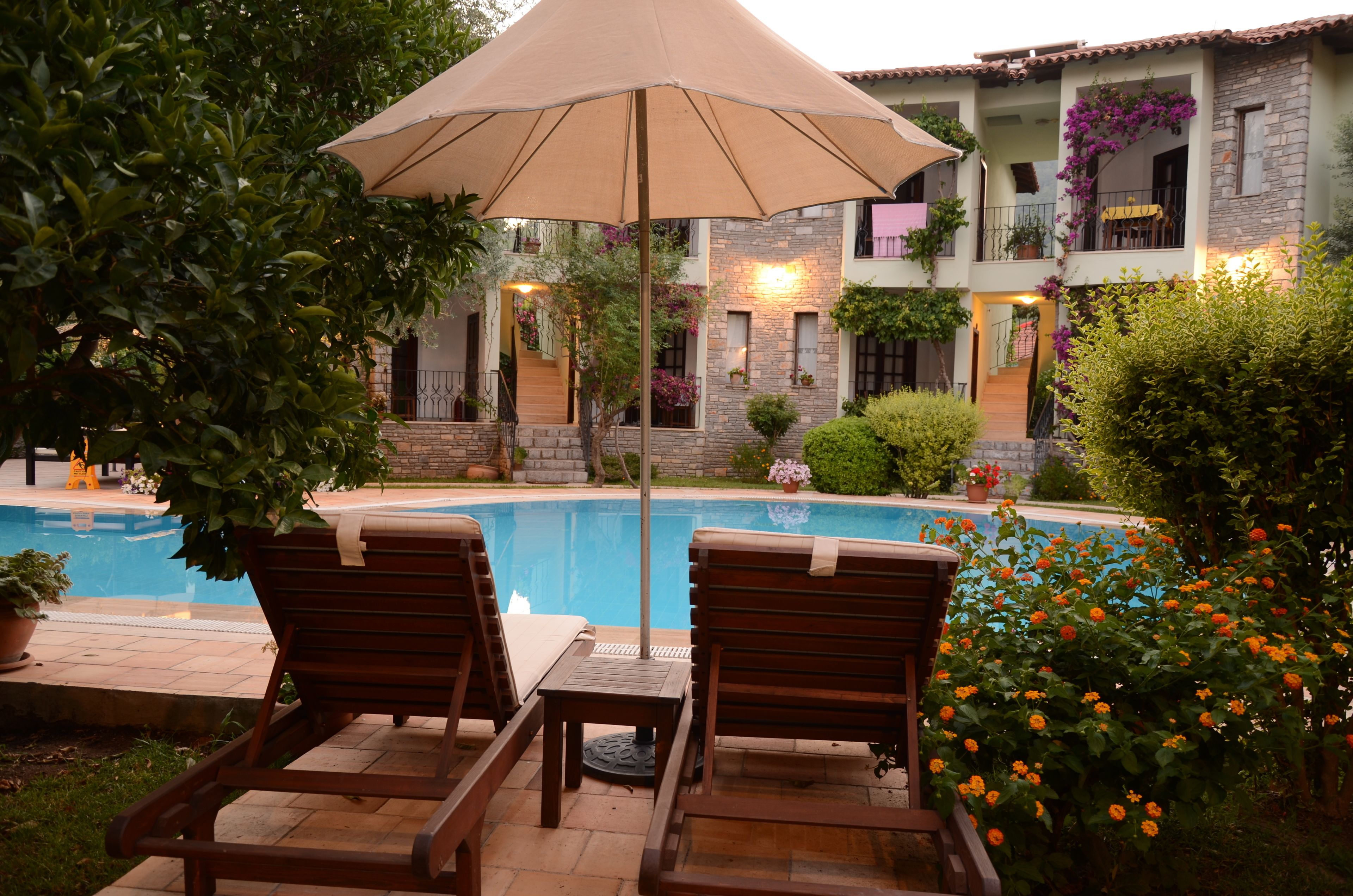 Un área junto a la piscina con dos sillones de madera, una mesa y una sombrilla grande.