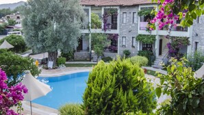 Un edificio in pietra con balconi, una piscina e vegetazione lussureggiante.