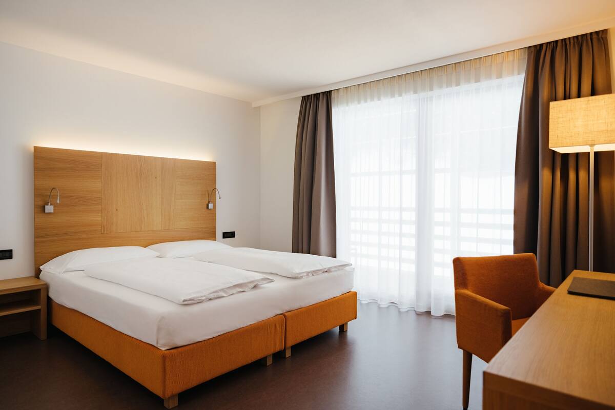 Une chambre d’hôtel avec une tête de lit en bois, un lit double avec du linge de lit blanc, un bureau en bois et une chaise.