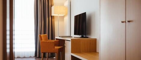 A hotel room with a wooden desk, a television, a chair, and a lamp.