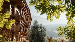 Une cabane en bois dotée d’un balcon, entourée d’arbres et avec des montagnes en arrière-plan.