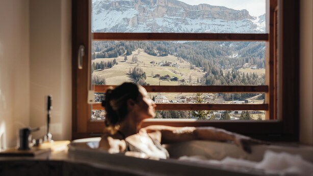 Une personne allongée dans son lit, avec vue sur un paysage montagneux par la fenêtre.