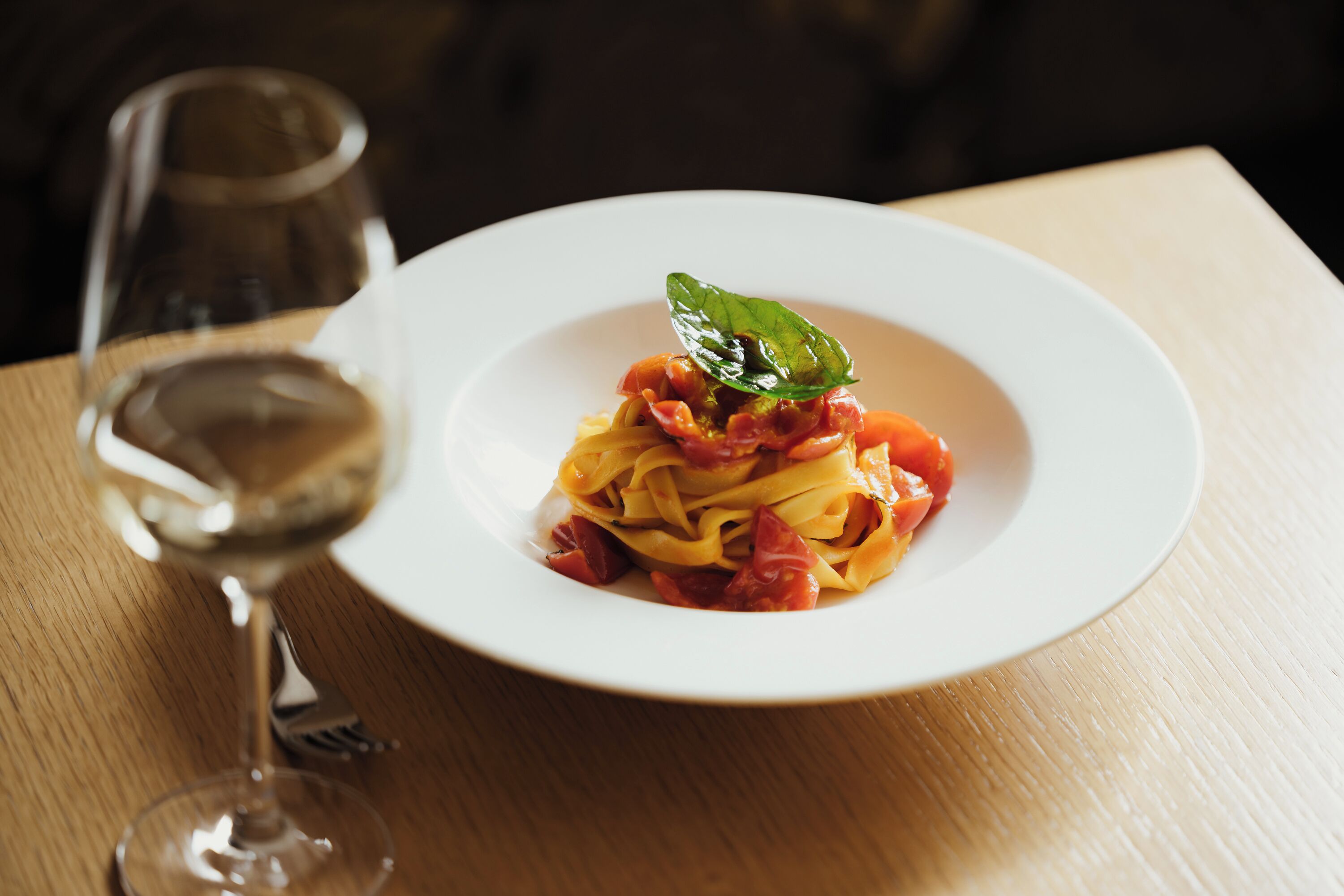 A plate of pasta with a basil leaf garnish on a wooden table.