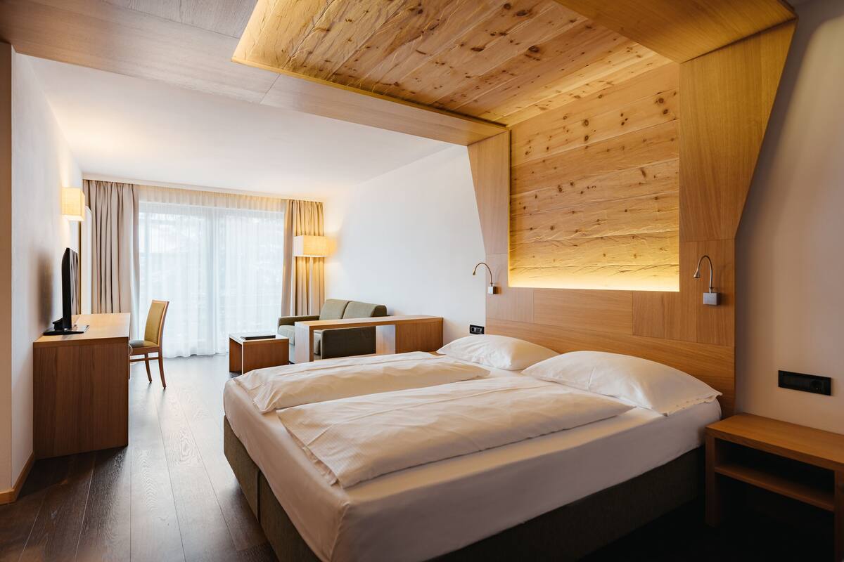 Une chambre d’hôtel moderne avec un plafond en bois, un grand lit avec du linge de lit blanc, un bureau avec une chaise et un téléviseur.