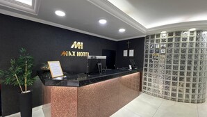 A hotel reception desk with a black and copper color scheme, a plant, and a glass display wall. - Max Hotel (Nucleo Bandeirante)