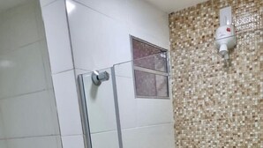 A bathroom with a glass shower enclosure, a toilet, and a tiled wall with a mosaic pattern. - Max Hotel (Nucleo Bandeirante)