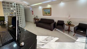 A reception area with a black reception desk, a brown sofa, two armchairs, a small round table with an orchid, and a painting on the wall. - Max Hotel (Nucleo Bandeirante)