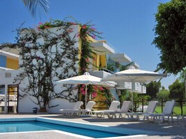 Un área de piscina con sillones blancos y sombrillas, rodeada por un edificio con plantas trepadoras y flores.