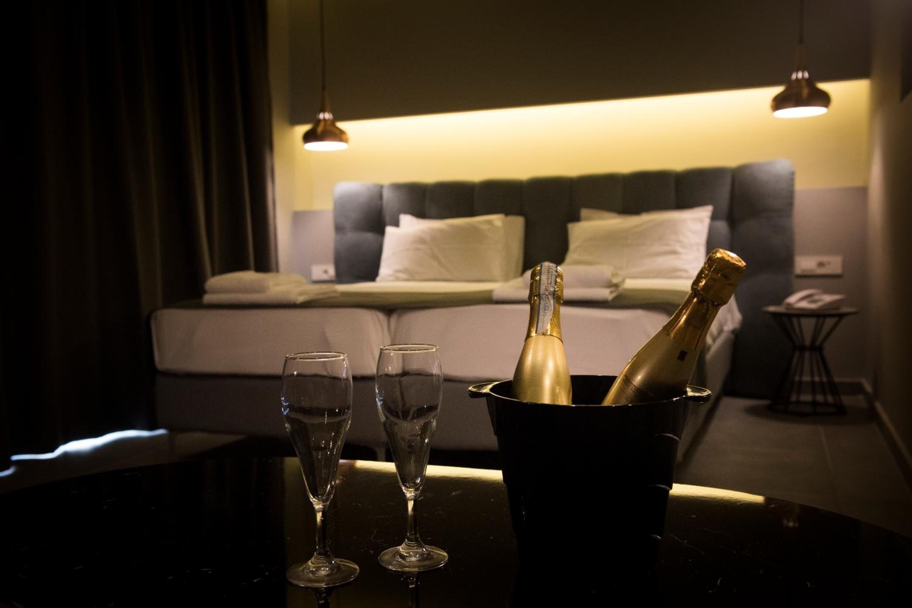 Ein Zimmer mit einem Bett, einem Nachttisch und einem Tisch mit zwei Gläsern und einer Champagnerflasche in einem Kübel.