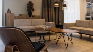 Una sala moderna con sofá, mesa de centro y sillones. Hay lámparas colgantes y un ventanal con cortinas.