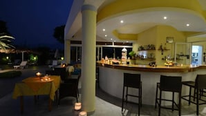 Zona de bar exterior con barra curva, asientos y vistas al área de la piscina al anochecer.