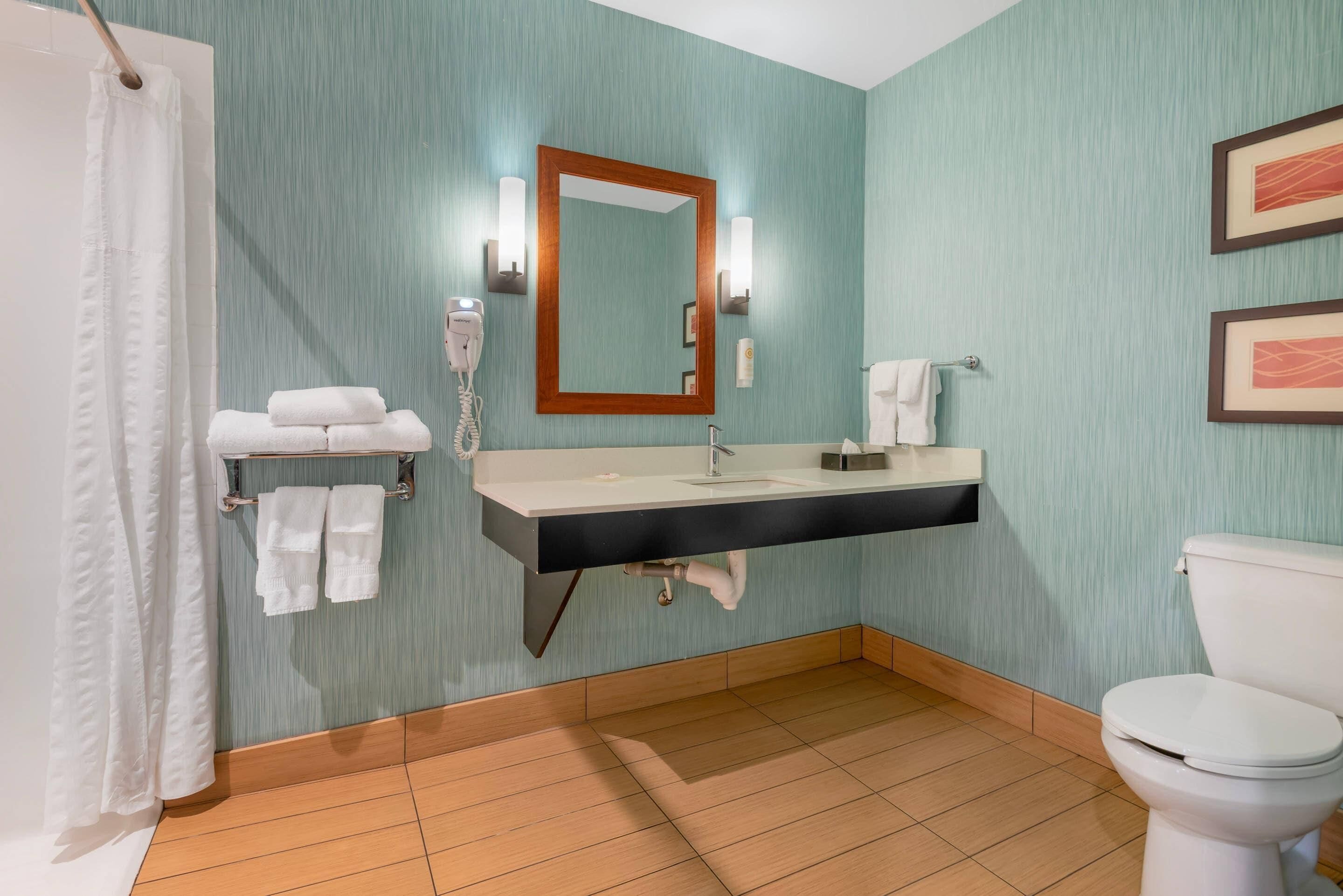A bathroom with a sink, mirror, towel rack, toilet, and shower curtain.