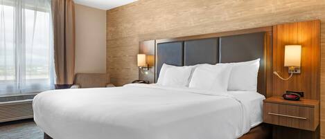 A hotel room with a large bed, wooden headboard, bedside lamps, and a view of the city.