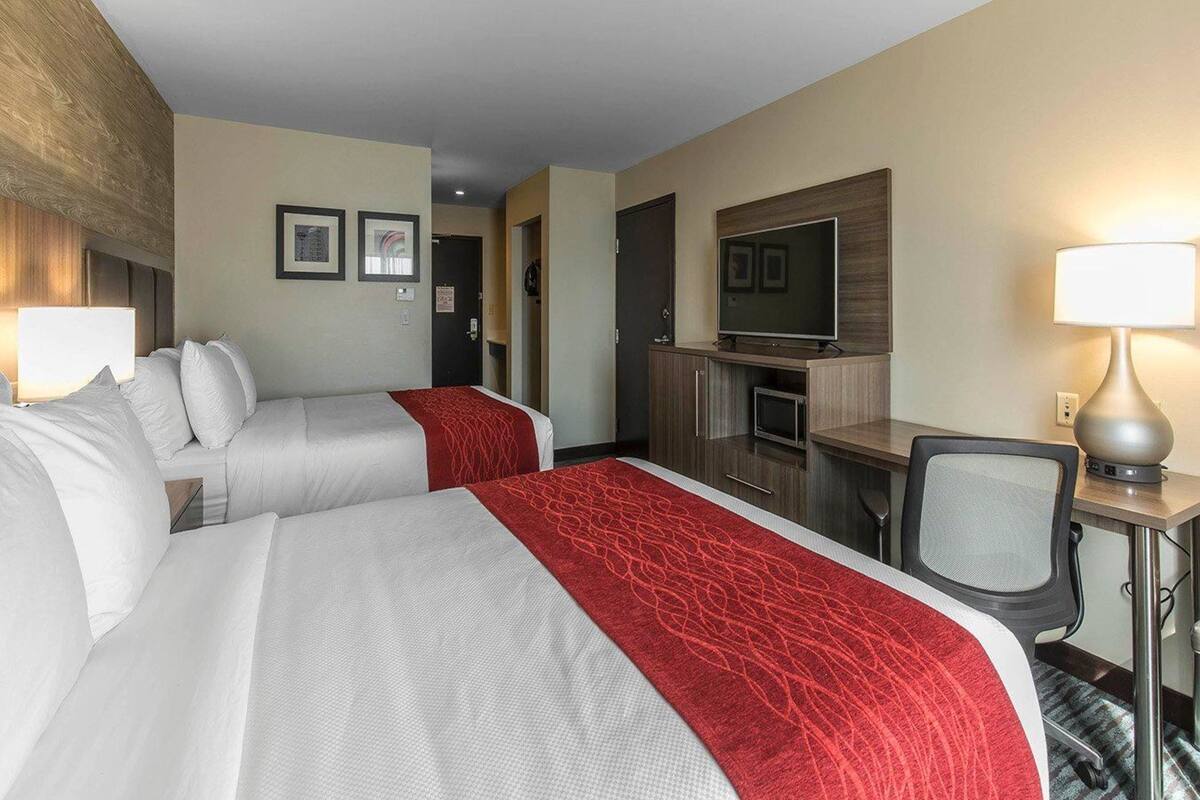 A hotel room with two beds, a TV, a desk, and a chair.