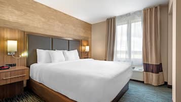 Una habitación de hotel con una cama grande, cabecera de madera, dos lámparas de noche, una mesita de noche y una ventana con cortinas.
