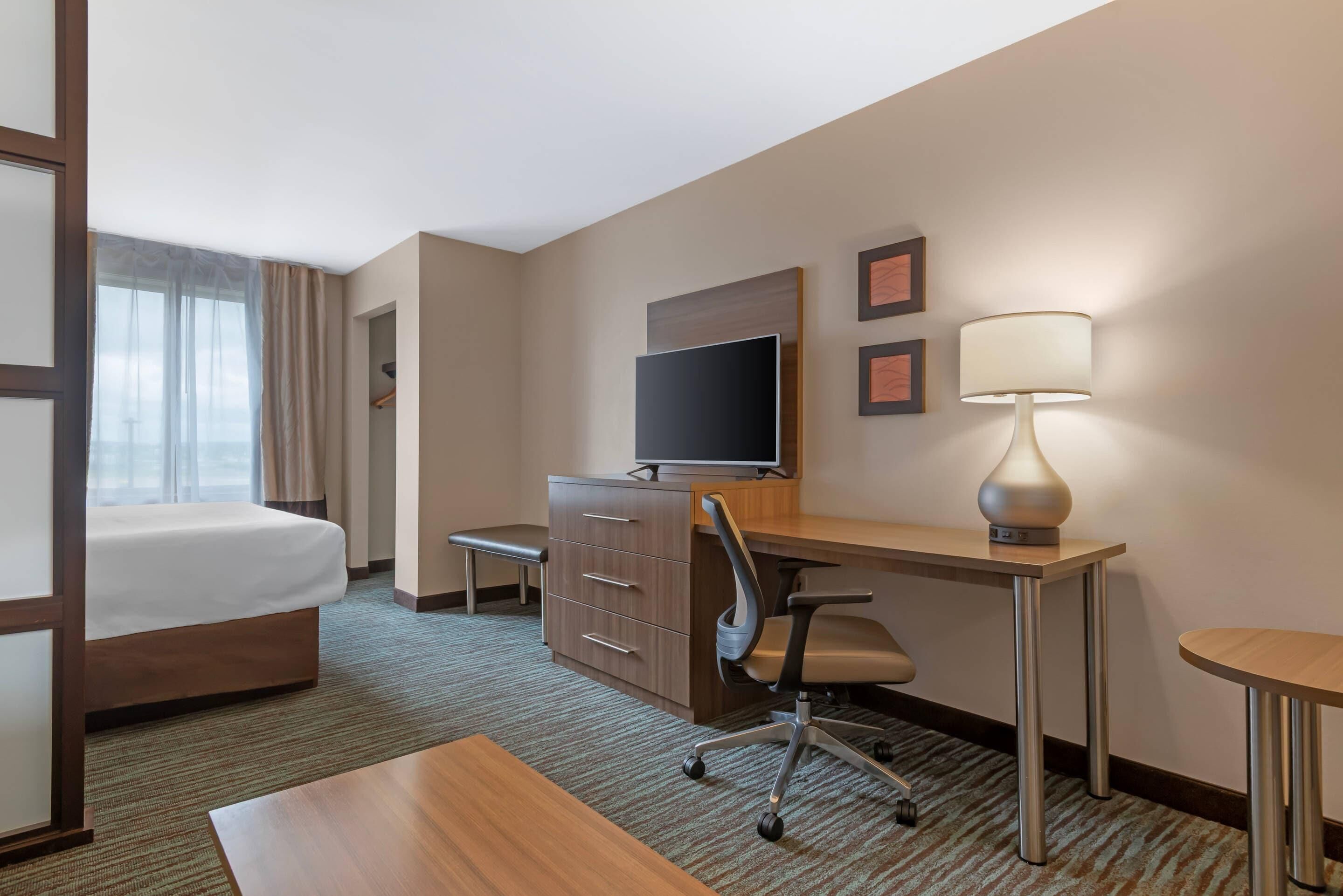A hotel room with a bed, desk, chair, TV, lamp, and a view of the outdoors.