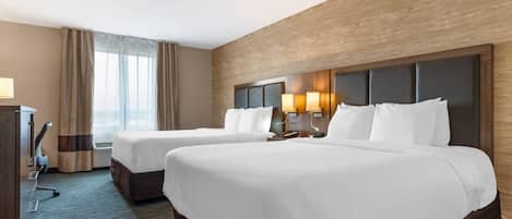A hotel room with two beds, a desk, a lamp, and a window with curtains.