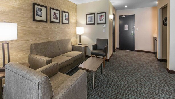 A hotel room with a sofa, armchair, and a small table. There are framed pictures on the wall and a door in the background. - Comfort Inn & Suites Airport North (Calgary)