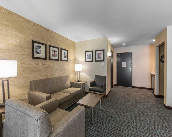 A hotel room with a sofa, armchair, and a small table. There are framed pictures on the wall and a door in the background. - Comfort Inn & Suites Airport North (Calgary)