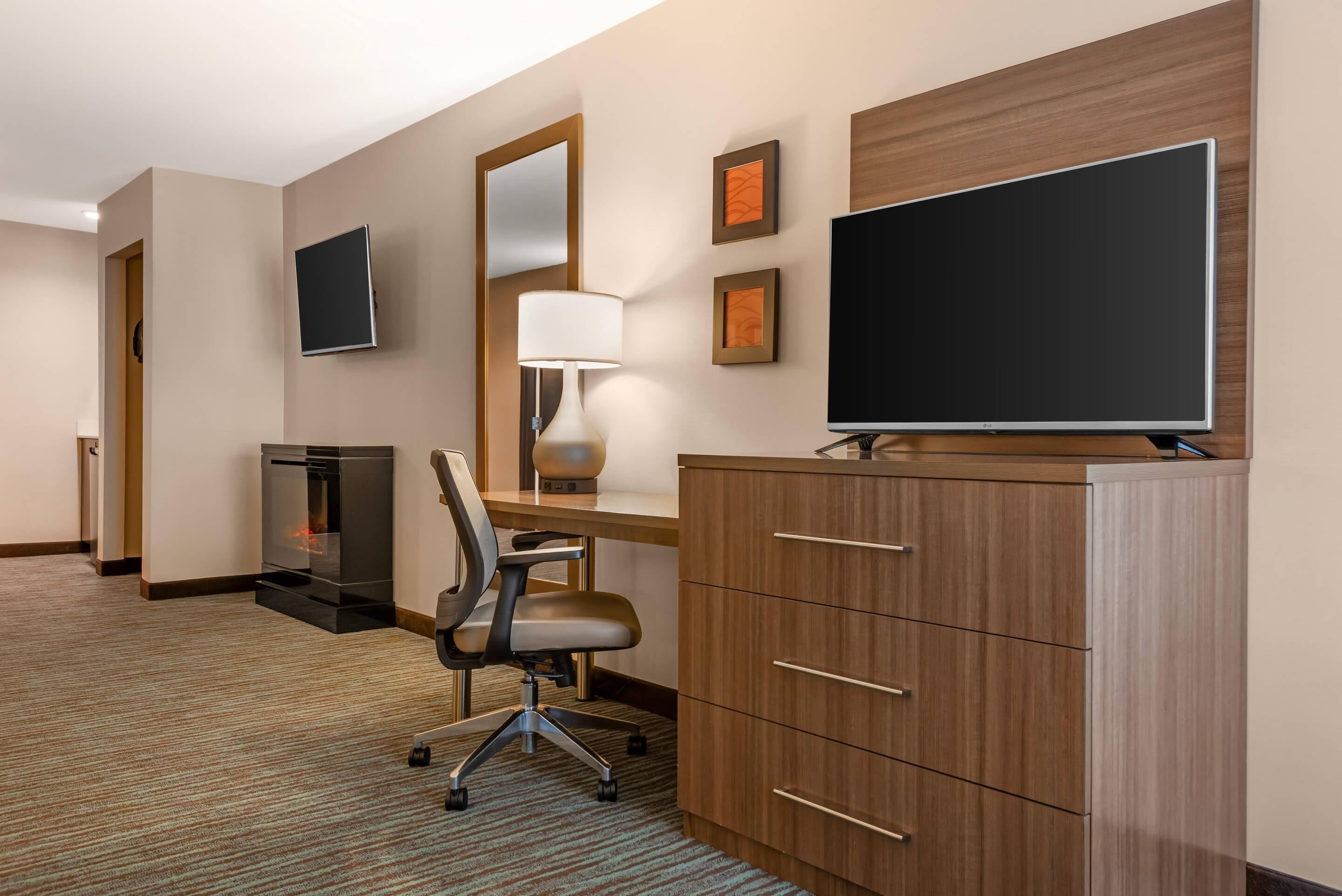 Habitación de hotel con escritorio de madera, televisor, chimenea y un espejo grande.