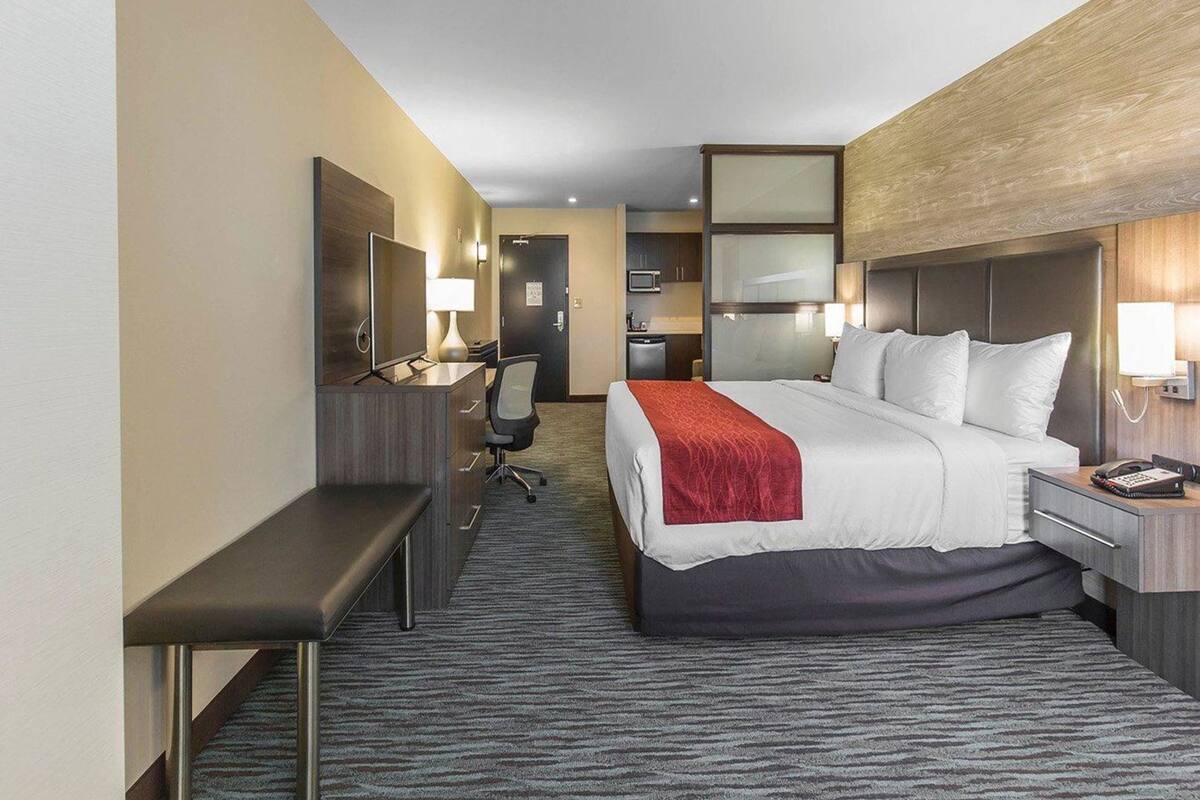 A hotel room with a bed, desk, chair, and a small kitchenette.