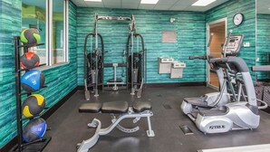 A gym with exercise equipment, a bench, a treadmill, and a wall clock. - Comfort Inn & Suites Airport North (Calgary)