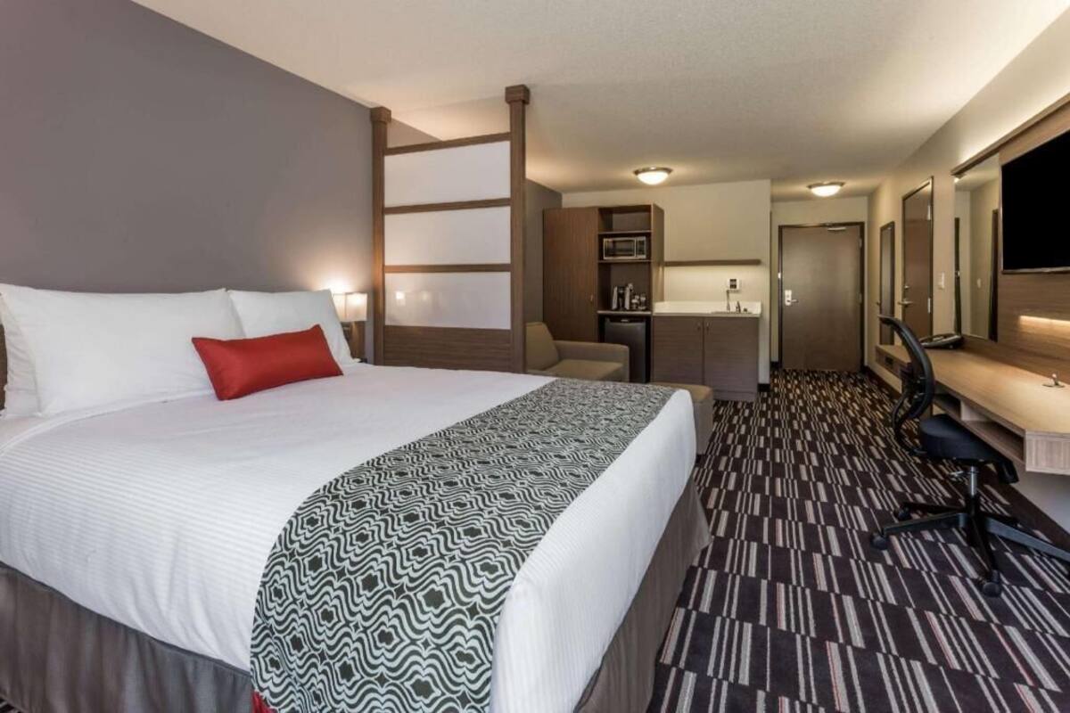 Una habitación de hotel con cama, escritorio, silla, microondas y televisor.