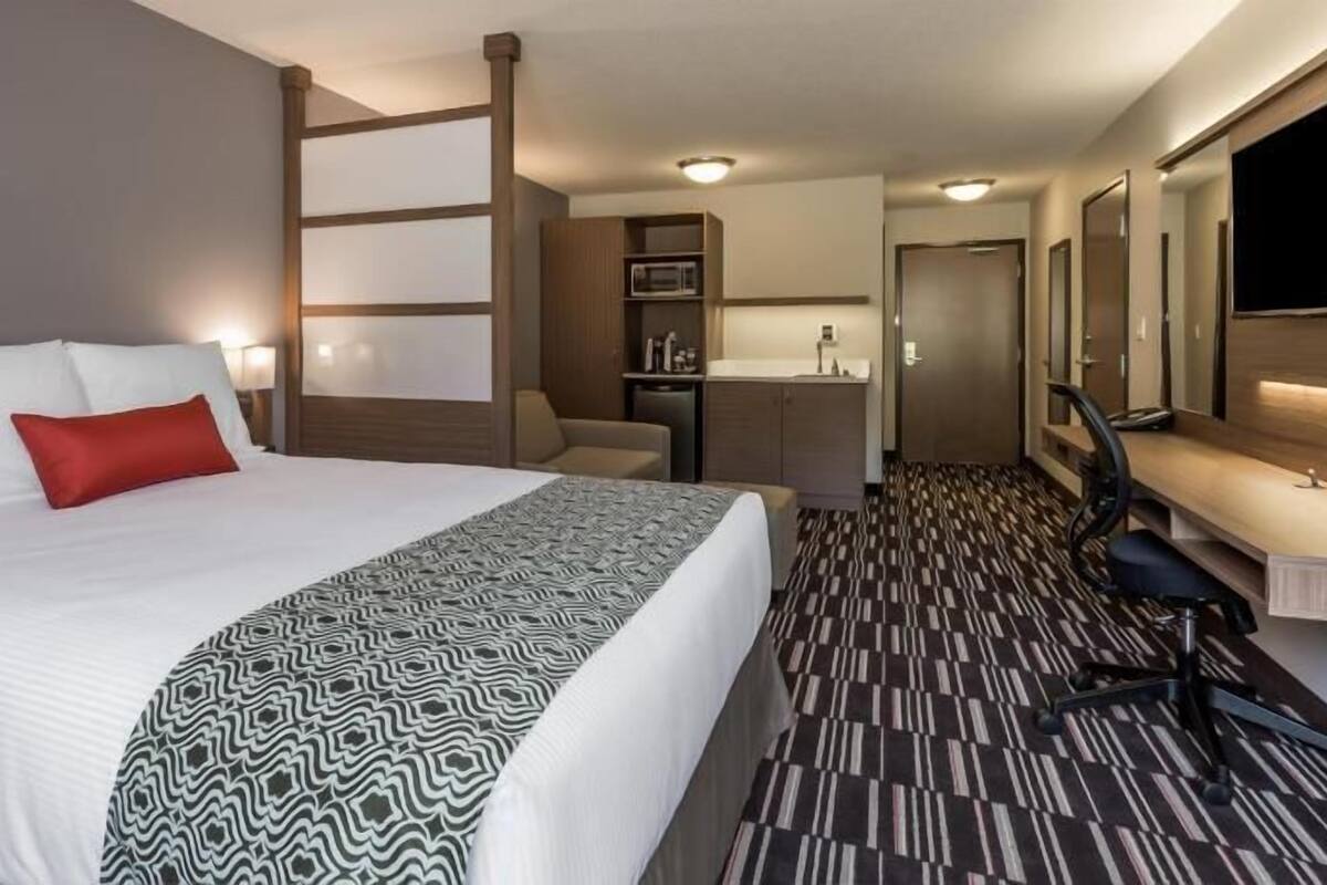 Habitación de hotel con una cama grande, un escritorio, una silla, kitchenette y baño.