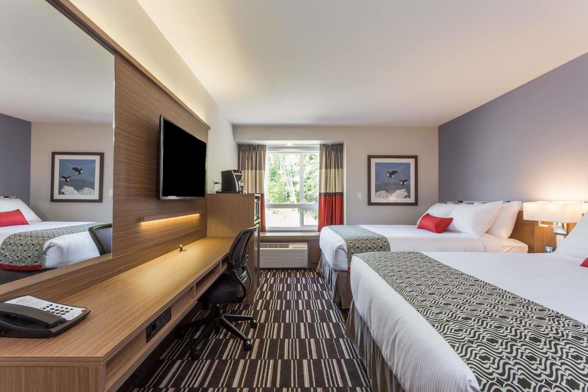 Una habitación de hotel con dos camas, un escritorio, una silla, un televisor y una ventana con cortinas.