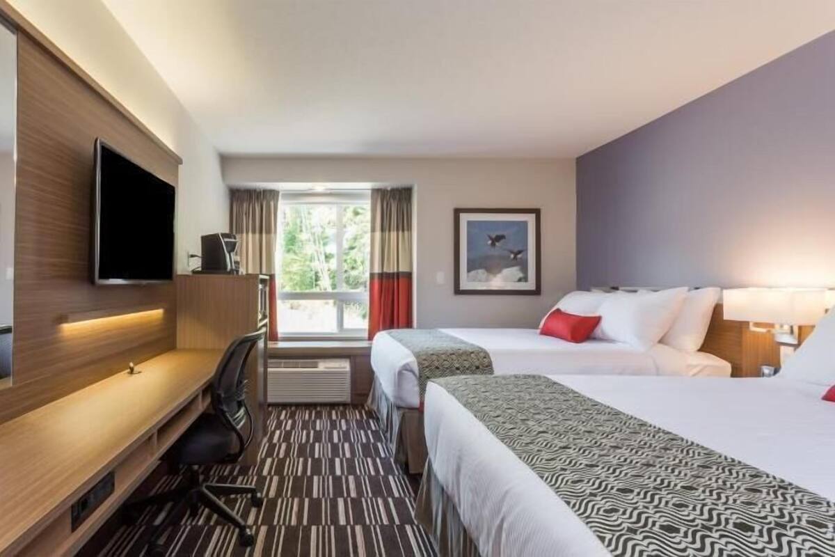 Habitación de hotel con dos camas, televisión, escritorio y ventana con cortinas.