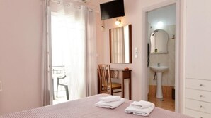 A bedroom with a bed, a chair, a desk, a TV, and a bathroom with a sink and mirror. - Villa Plaza (Spetses)