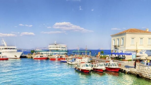 A marina with various boats docked, a large white building, and a smaller building with a red roof. - Villa Plaza (Spetses)