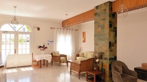 A spacious living room with a white door, a stone accent wall, and a wooden ceiling. - Villa Plaza (Spetses)