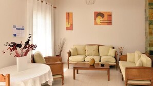 A living room with a sofa, two armchairs, a coffee table, and a dining table with a vase of flowers. - Villa Plaza (Spetses)