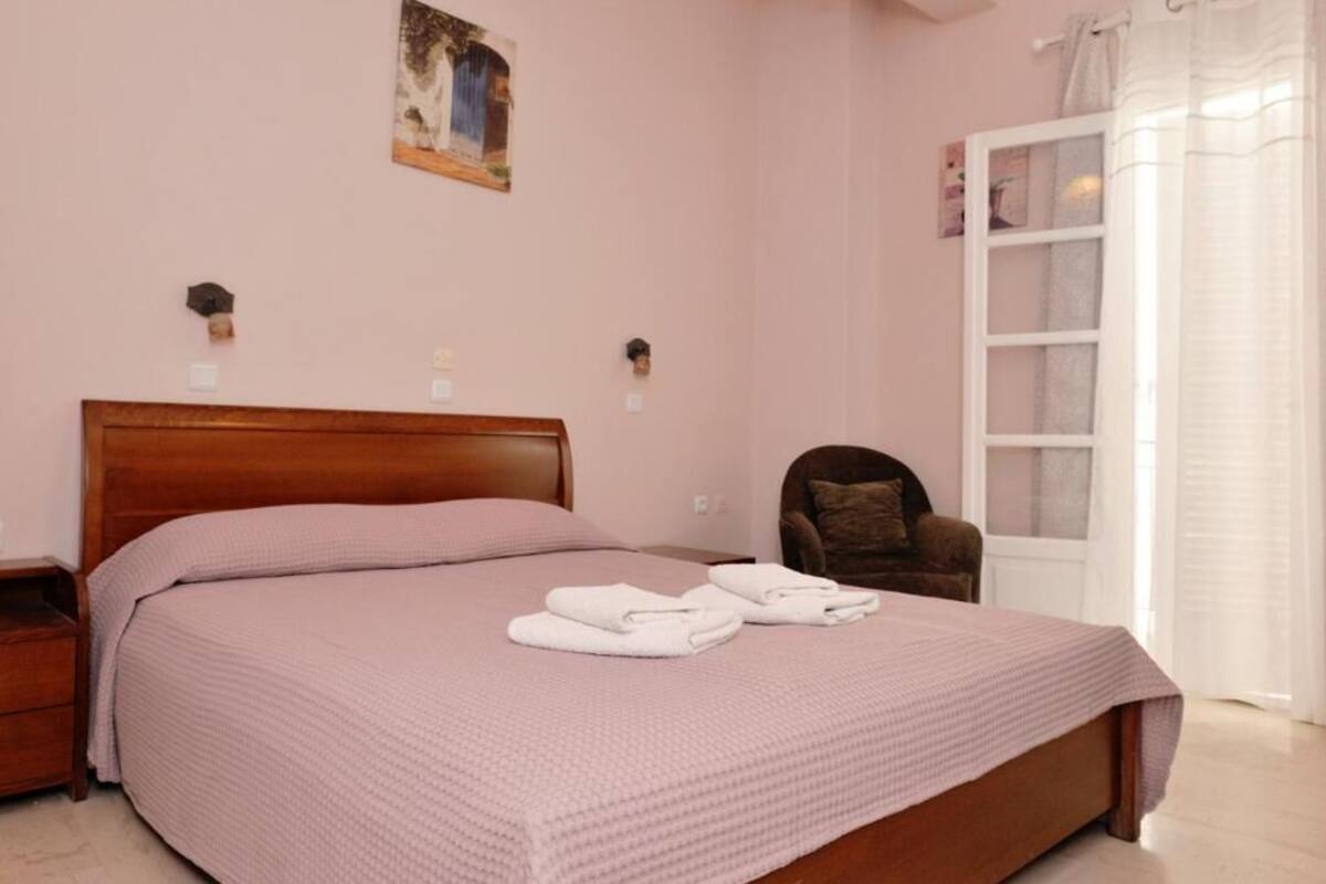 Un dormitorio con cama de madera, mesita de noche, una silla y ventana con cortinas.