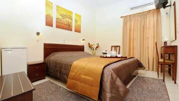 Habitación de hotel con cama, escritorio, silla, televisor y ventana con cortinas.