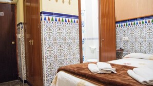 Une chambre d’hôtel avec un lit, une armoire en bois et une salle de bain aux carreaux décoratifs.