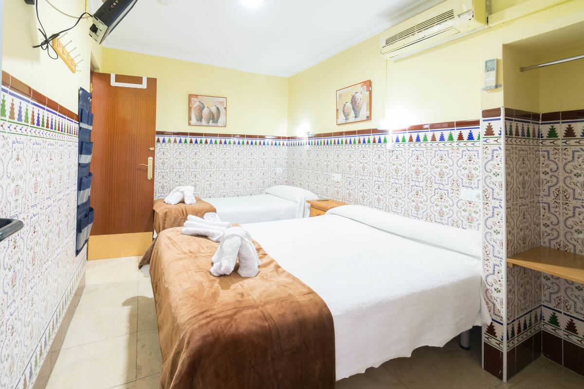 Habitación de hotel con dos camas, una puerta de madera, paredes con diseño y un estante pequeño.